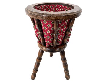May include: A wooden plant stand with three legs and a red fabric liner. The stand is made of dark wood and has a simple design.