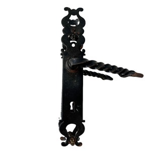 Peut inclure: Poignée de porte en métal noir avec un design torsadé et des détails ornés. La poignée est fixée à une plaque rectangulaire avec un trou de serrure.