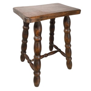May include: A dark brown wooden stool with a rectangular top and turned legs. The legs are connected by a stretcher.