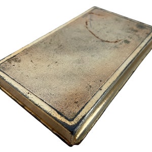 May include: A vintage, rectangular, gold-colored metal box with a worn, textured surface and a dark brown border.