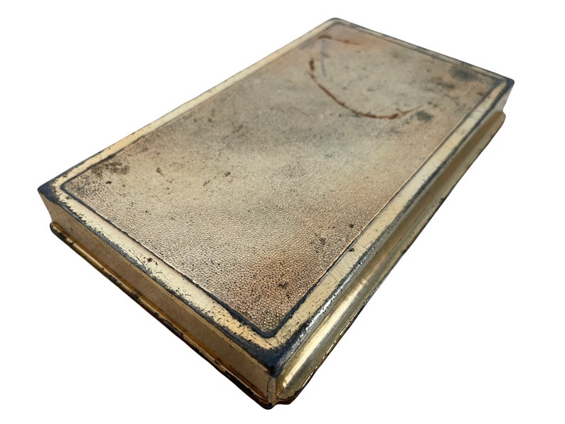 May include: A vintage, rectangular, gold-colored metal box with a worn, textured surface and a dark brown border.
