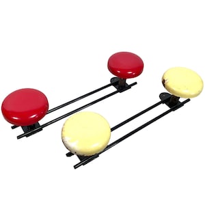 Peut inclure: Un ensemble de quatre tabourets métalliques vintage avec des sièges rouges et jaunes. Les tabourets sont fixés à une barre en métal noir.
