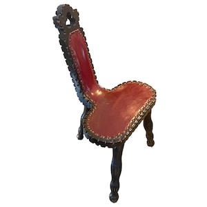 May include: A vintage wooden chair with a red leather seat and a unique, carved design. The chair has a high back and three legs.
