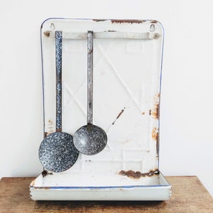Peut inclure: Étagère de cuisine en émail blanc avec une bordure bleue et deux louches en métal suspendues avec un émail noir et blanc moucheté. L'étagère a une petite étagère en bas.
