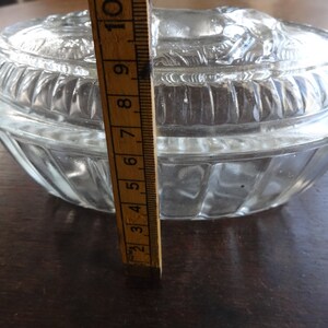 May include: A clear glass oval-shaped dish with a raised, textured lid. The dish is approximately 6 inches in diameter.