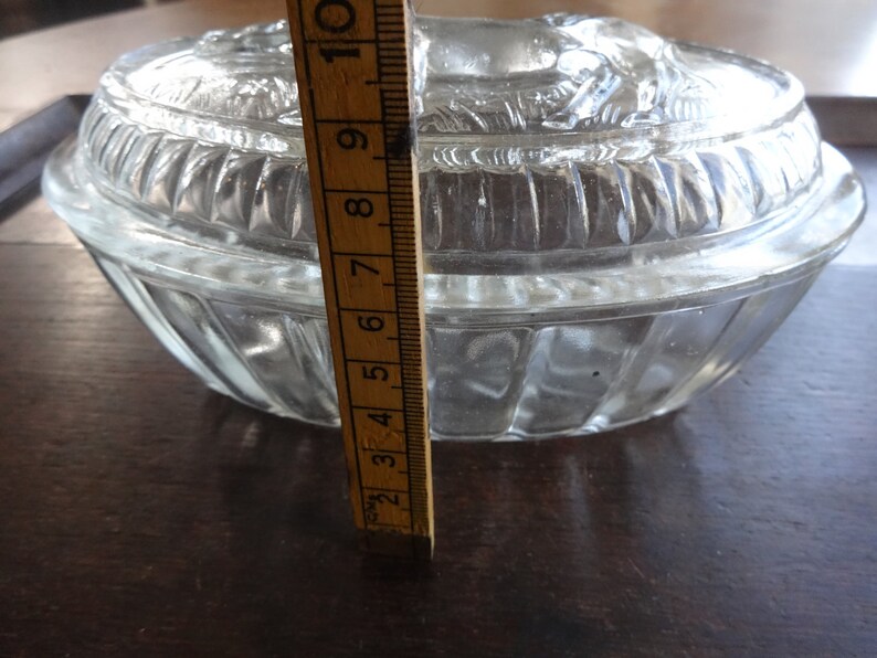 May include: A clear glass oval-shaped dish with a raised, textured lid. The dish is approximately 6 inches in diameter.