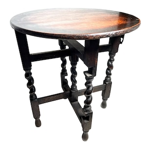 May include: A dark wood round table with a turned leg design. The table has a simple, rustic look and is perfect for a small space.