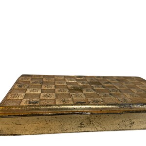 May include: A gold metal box with a checkered pattern on the top. The box has a slightly worn look.