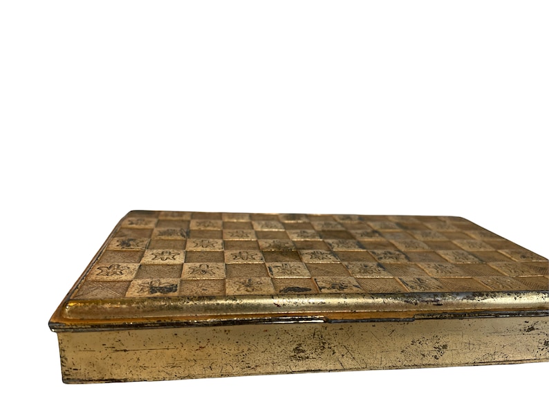 May include: A gold metal box with a checkered pattern on the top. The box has a slightly worn look.