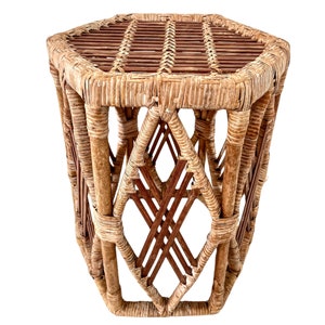 May include: A hexagonal wicker side table with a woven top and a diamond-shaped pattern on the sides. The table is made of natural brown wicker.