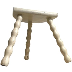 Puede incluir: Un taburete de madera blanco con tres patas retorcidas. El taburete está hecho de madera y tiene un diseño sencillo.