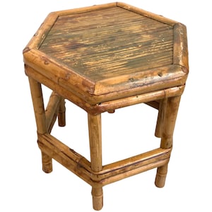 Puede incluir: Una mesa auxiliar hexagonal de bambú con un acabado natural. La mesa tiene un aspecto desgastado con una pátina ligeramente verde. La mesa mide aproximadamente 46 cm de alto.