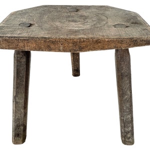 May include: A rustic wooden stool with a square top and three legs. The stool is made of weathered wood and has a natural finish.