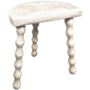 May include: White wooden stool with a half-round top and three legs. Each leg is made of a series of rounded knobs.