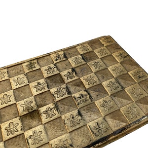May include: A gold-colored metal box with a checkered pattern and a floral design. The box has a slightly worn look.