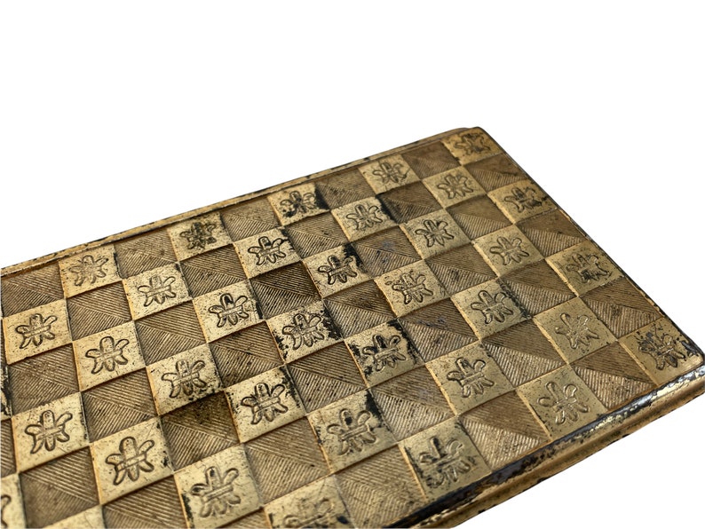 May include: A gold-colored metal box with a checkered pattern and a floral design. The box has a slightly worn look.