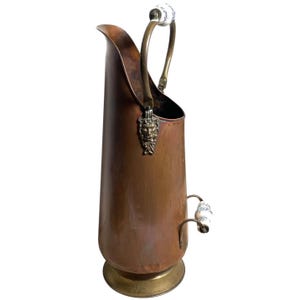 May include: A copper coal scuttle with brass accents and porcelain handles. The scuttle features a lion's head design on the front.