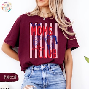 Pode incluir: Camiseta bord&ocirc; com a frase "the Moms Coffee Club" em vermelho e azul, com um desenho de cafeteira. A camiseta tem um design listrado e &eacute; feita de um material macio.