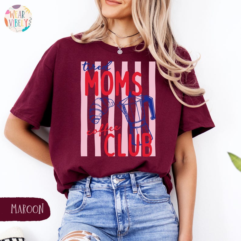 Pode incluir: Camiseta bord&ocirc; com a frase "the Moms Coffee Club" em vermelho e azul, com um desenho de cafeteira. A camiseta tem um design listrado e &eacute; feita de um material macio.
