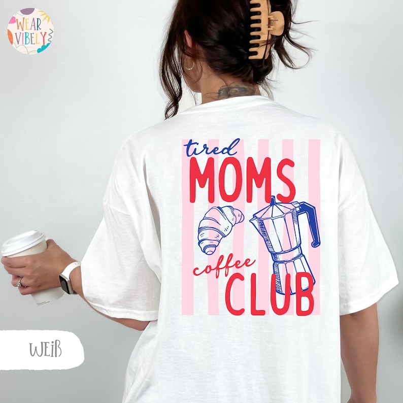 Pode incluir: Camiseta branca com um gr&aacute;fico nas costas que diz "tired MOMS coffee CLUB" em vermelho e azul. O gr&aacute;fico inclui um croissant e uma cafeteira. A camiseta tem um corte folgado.