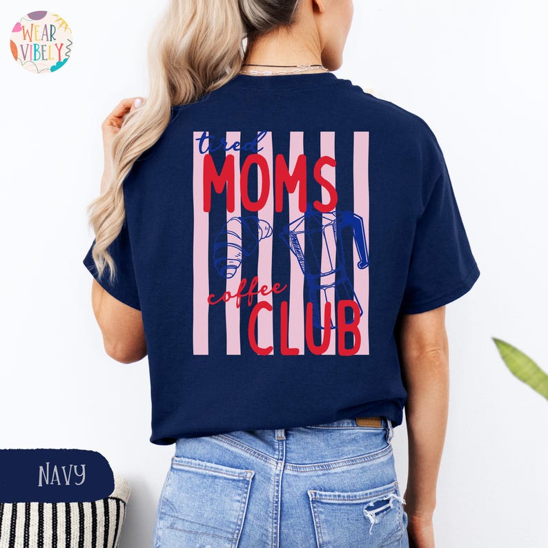 Pode incluir: Camiseta azul marinho com a frase "tired MOMS coffee CLUB" em vermelho e branco, com um desenho de cafeteira. O desenho est&aacute; nas costas da camisa, com listras verticais rosa e brancas.