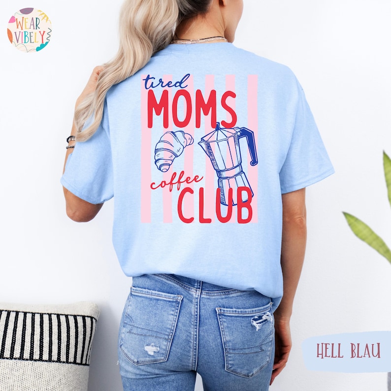 Pode incluir: Camiseta azul claro com o texto "tired MOMS coffee CLUB" em vermelho e azul. O design inclui um croissant e uma cafeteira. A parte de tr&aacute;s da camiseta tem listras verticais rosa e brancas.