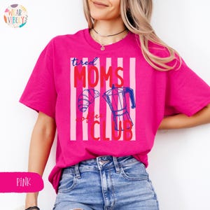 Pode incluir: Uma t-shirt rosa choque com o texto "tired MOMS coffee CLUB" em vermelho e azul, com um croissant e uma cafeteira. A t-shirt &eacute; de uma cor rosa vibrante.
