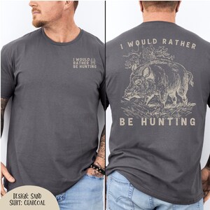 May include: Charcoal gray t-shirt with the text "I WOULD RATHER BE HUNTING" on the front and back. The back of the shirt features a detailed illustration of a boar. The design is in sand color.