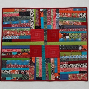 Könnte beinhalten: Ein roter, grüner, blauer und schwarzer Patchwork-Decken mit geometrischem Muster. Die Decke besteht aus verschiedenen Stoffen und hat einen modernen, abstrakten Look.