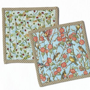 Könnte beinhalten: Zwei gequiltete Topflappen mit einem braunen und weißen Gingham-Rand. Ein Topflappen hat einen blauen Hintergrund mit einem Blumenmuster und Vögeln. Der andere Topflappen hat einen blauen und weißen Hintergrund mit einem Gänseblümchen- und Marienkäfermuster.