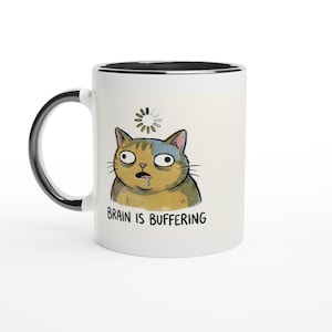 Puede incluir: Taza de cerámica blanca con asa y borde negros. La taza presenta un gato de dibujos animados con una expresión angustiada y el texto "BRAIN IS BUFFERING". El gato es amarillo, azul y marrón.