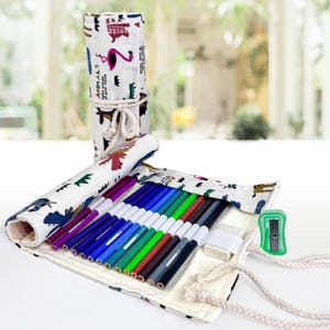 May include: A rolled-up canvas pencil case with a white background and animal print. The case is unrolled, revealing a collection of colorful markers, an eraser, and a green pencil sharpener. The case is tied with a white rope.