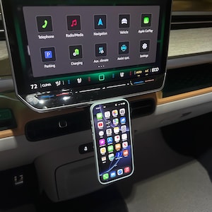 Puede incluir: Un tel&eacute;fono inteligente con una funda verde claro est&aacute; montado en un coche. La pantalla del tel&eacute;fono muestra iconos de aplicaciones. El salpicadero del coche tiene una gran pantalla t&aacute;ctil que muestra la navegaci&oacute;n y la informaci&oacute;n del veh&iacute;culo. La temperatura es de 28 grados Celsius.