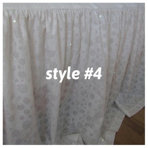 May include: White bed skirt with a ruffled edge and a subtle pattern. The skirt has a white background with a light gray pattern and is decorated with small, iridescent sequins. The text "style #4" is printed in black on the skirt.