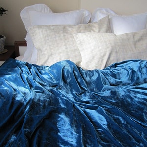 May include: A blue velvet duvet cover with a white and beige patterned pillow on top. The duvet cover is folded back to reveal the blue velvet fabric.