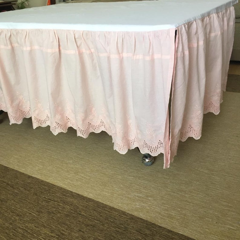 May include: A pink bed skirt with a white lace trim. The skirt is gathered and has a ruffled edge.