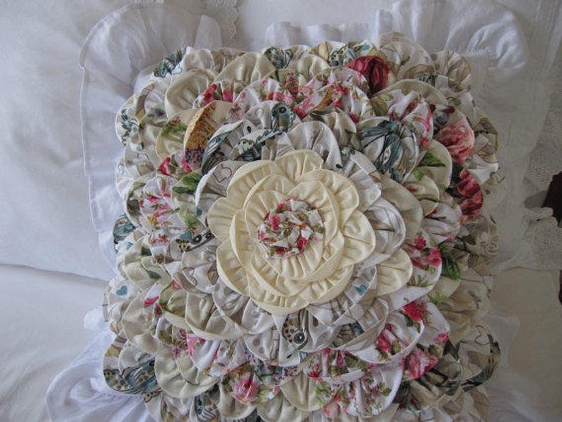 May include: A decorative pillow with a large, cream-colored flower in the center surrounded by smaller, multi-colored floral fabric rosettes.