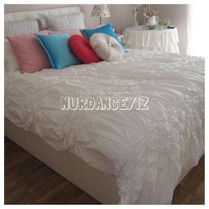 May include: White ruffled bedspread with a pink, blue, and red throw pillows on a white bed with a white headboard.