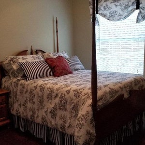 May include: A white and black floral patterned bedspread with a black and white striped bed skirt. The bed has a wooden headboard with tall posts and a red and white patterned pillow.