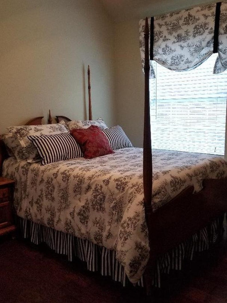May include: A white and black floral patterned bedspread with a black and white striped bed skirt. The bed has a wooden headboard with tall posts and a red and white patterned pillow.