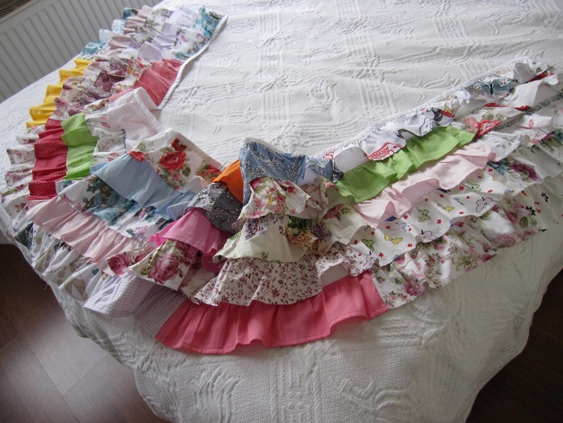 May include: A white bedspread with a colorful ruffled trim made from various patterned fabrics. The trim is made of multiple layers of fabric in different colors and patterns, including floral, paisley, and polka dots.
