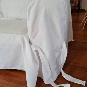 May include: White sofa slipcover with a fitted back and a gathered skirt. The slipcover has two long ties that can be tied around the legs of the sofa.