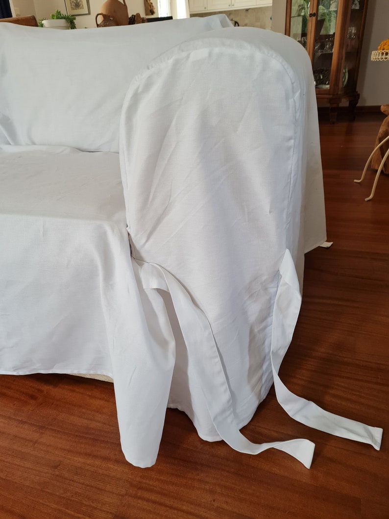 May include: White sofa slipcover with a fitted back and a gathered skirt. The slipcover has two long ties that can be tied around the legs of the sofa.