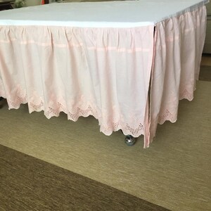 May include: A pink bed skirt with a white lace trim. The skirt is gathered and has a ruffled edge.