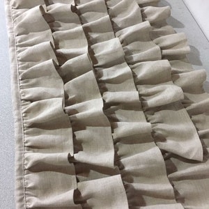 May include: A beige linen valance with multiple rows of ruffles. The valance is made of a soft, natural fabric and has a simple, elegant design.