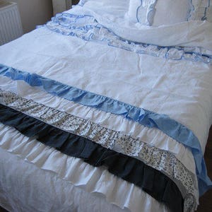 May include: A white bedspread with multiple layers of ruffles in blue, white, and black. The bedspread is made of a soft, linen-like fabric.