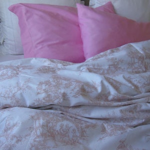 May include: A white bed with a floral pattern on the sheets. Two pink pillows are on the bed, one on top of the other.