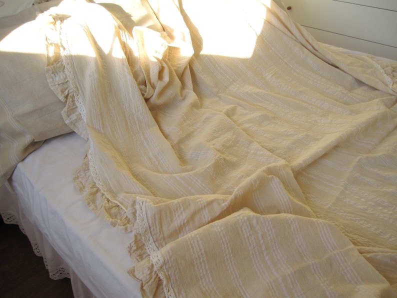 May include: A white bed with a white crocheted bedspread and a white pillow with lace trim. The bedspread is ruffled and has a textured pattern.