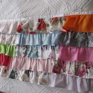May include: A multi-colored ruffled fabric trim with a variety of floral patterns, including pink, green, blue, red, and white.