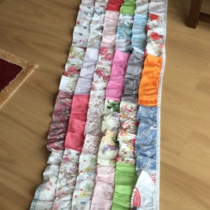 May include: A long, multi-colored fabric valance with a ruffled edge. The valance is made of various patterned fabrics, including floral prints, polka dots, and stripes. The valance is a patchwork of different fabrics, creating a unique and colorful design.